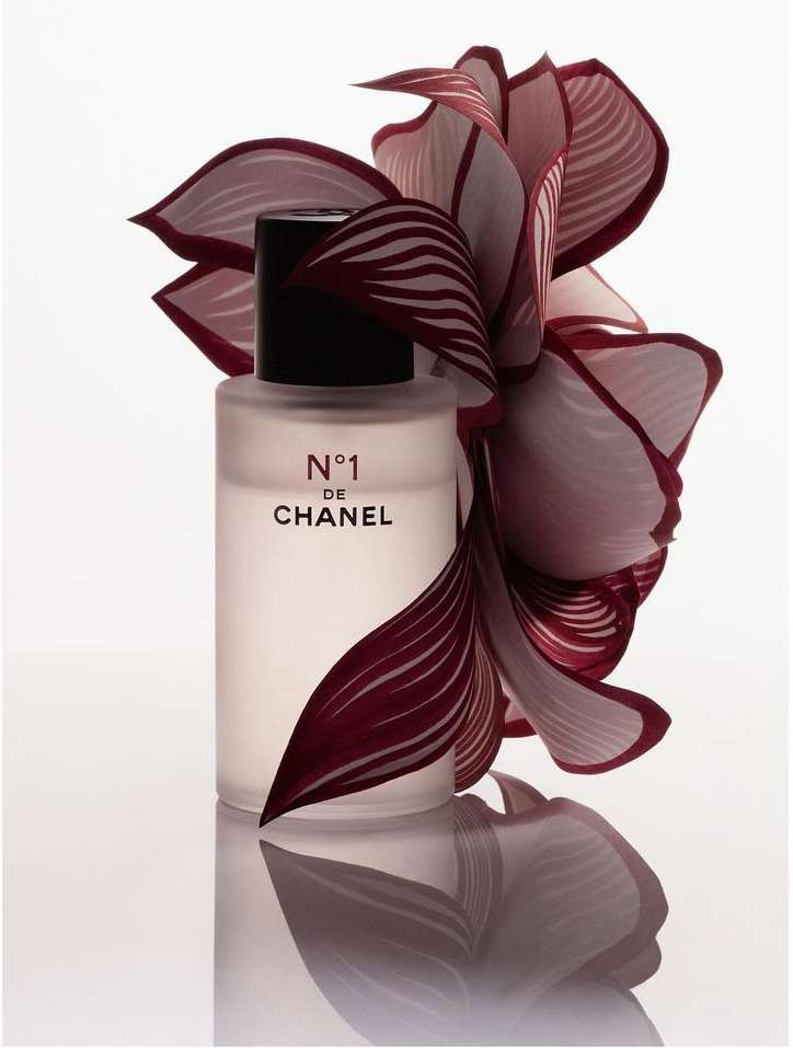 Frosted glass Chanel N°1 perfume bottle with black cap is adorned with striking reddish-purple patterned floral accents on a white surface.