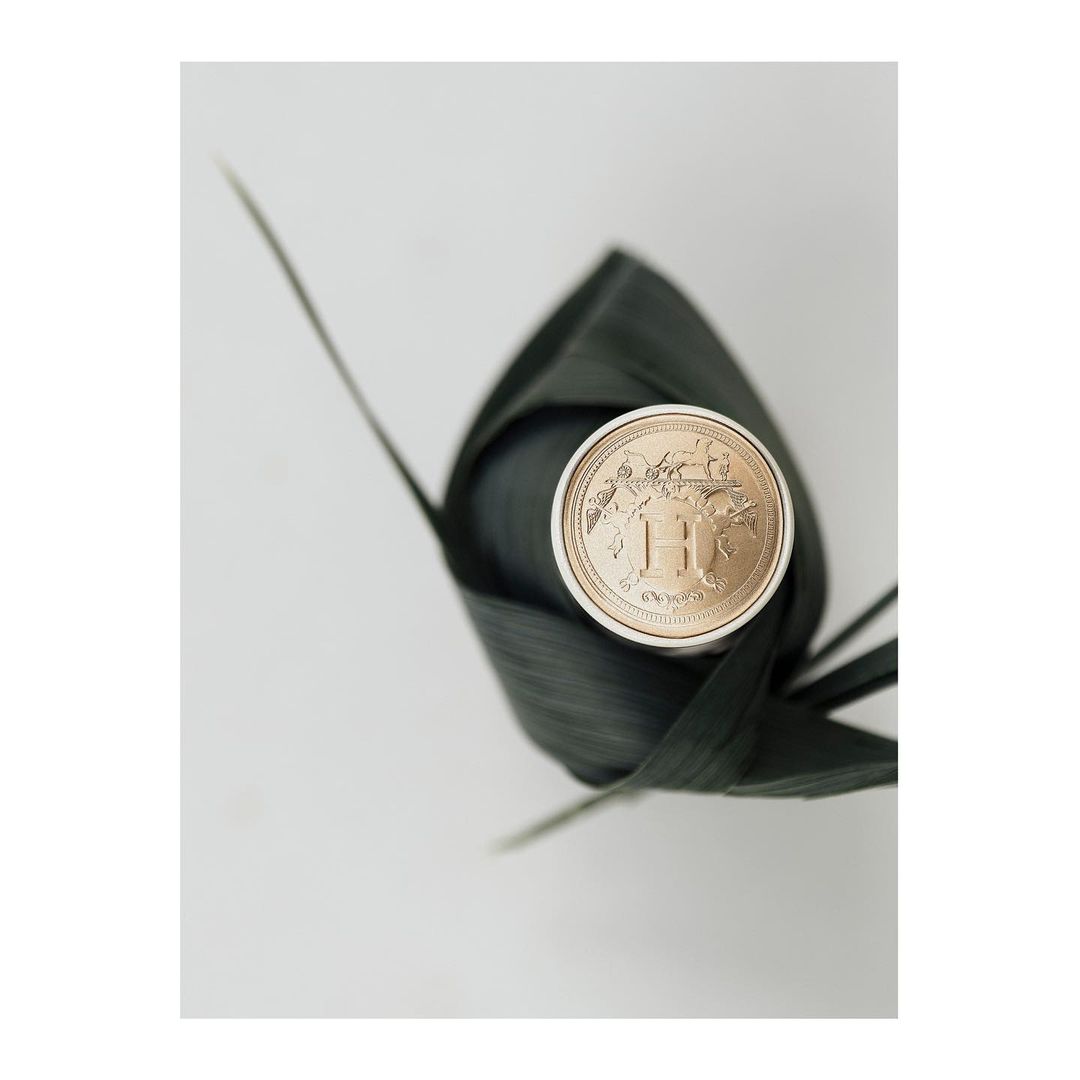 High-angle studio shot of a wrapped, round luxury soap or cosmetic product with gold emblem, encased in woven leaves on white surface.