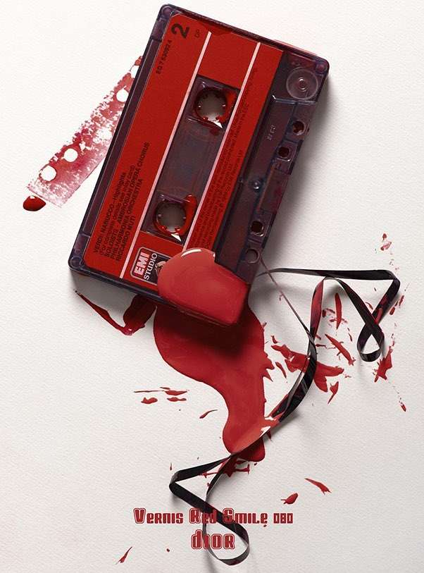 Still life of a red cassette tape with spilled red nail polish, creating an artistic composition on a white background.
