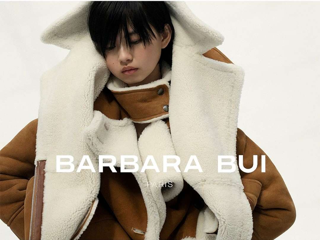 Woman poses in a Barbara Bui shearling coat against a bright background, showcasing high-fashion apparel with clear brand visibility.