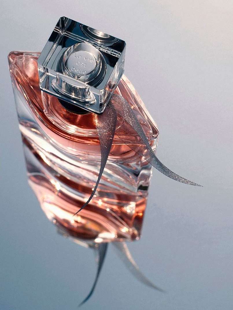 Elegant close-up studio shot of a luxury glass perfume bottle on a reflective surface with a decorative ribbon. Beauty and fragrance product.