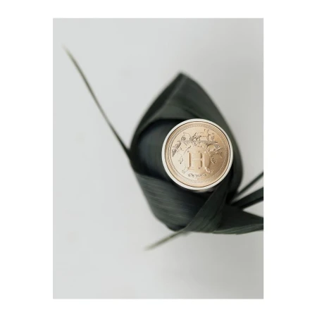 Close-up of a circular perfume cap with metallic gold branding wrapped neatly inside a dark green leaf on a light background