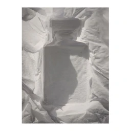 A perfume bottle wrapped inside crumpled white tissue paper, photographed in soft overhead lighting.