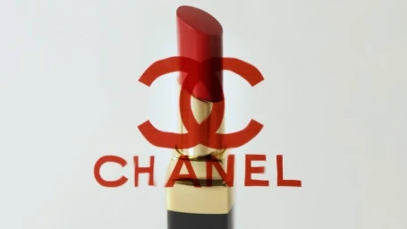 Close-up of a Chanel lipstick tube in red and gold against a neutral background with a red logo overlay.