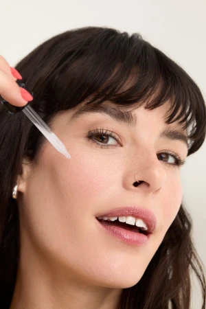 Close-up portrait of a woman applying skincare serum with a dropper near her cheek, captured by Beth Sternbaum.
