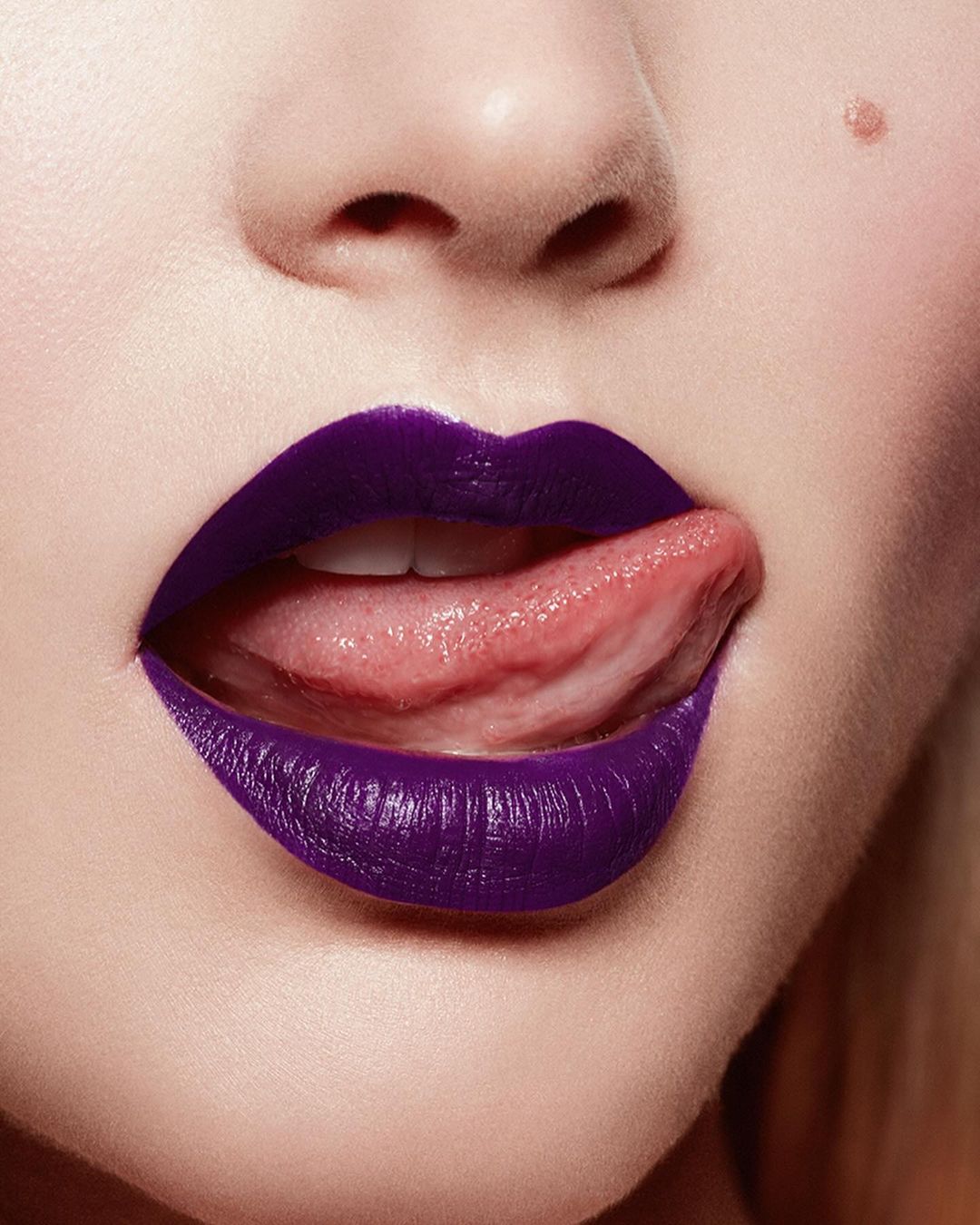 Close-up portrait of a fair-skinned person with dark purple lipstick, sticking their tongue out, with a clear focus on makeup and beauty.