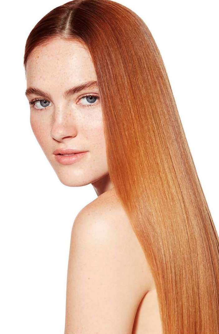 Portrait of a red-haired fair-skinned woman with bare shoulders against a bright white background, showcasing flawless complexion and hair.