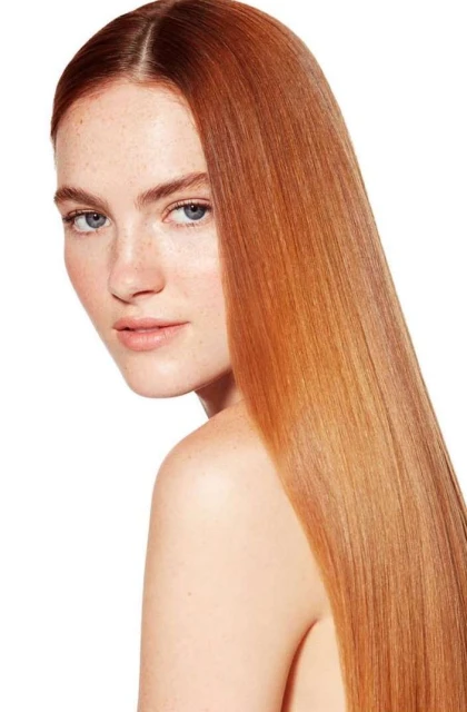 Portrait of a red-haired fair-skinned woman with bare shoulders against a bright white background, showcasing flawless complexion and hair.
