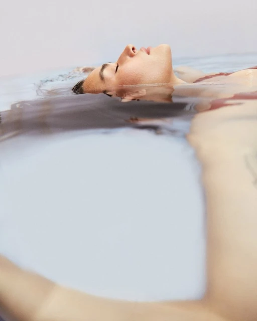 Adult female floats in calm water, eyes closed in relaxation, indoor setting, light complexion, fair lighting, horizontal orientation.