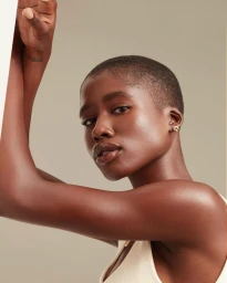 Close-up portrait of a Black woman with short hair posing with raised arms against a neutral background.