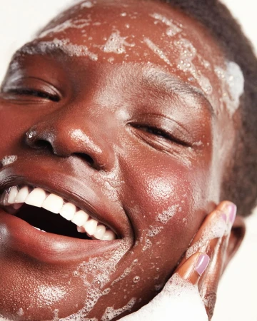 Close-up portrait of a smiling Black woman with suds and lather on her face, photographed by Beth Sternbaum.