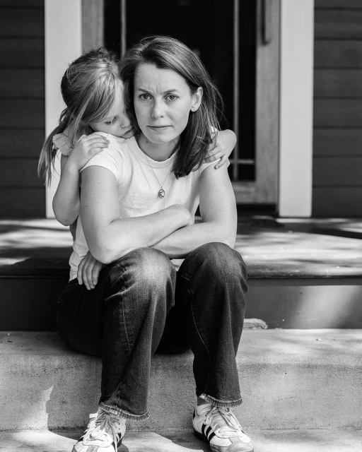 A mother and child are seated together on porch steps in a black and white photo, arms around each other in a loving embrace.