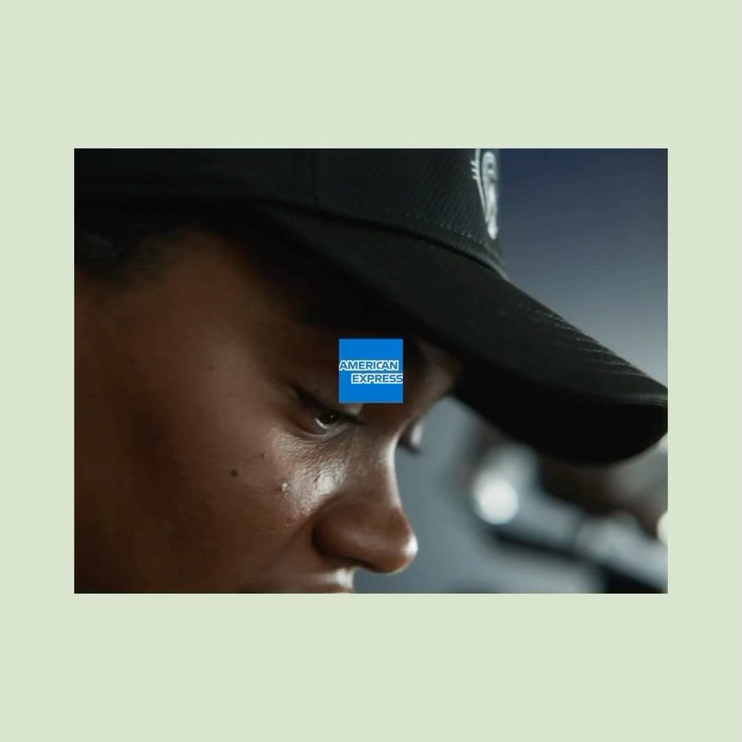 Close-up of an adult with dark hair wearing a baseball cap, showcasing a determined look. The American Express logo is visible.