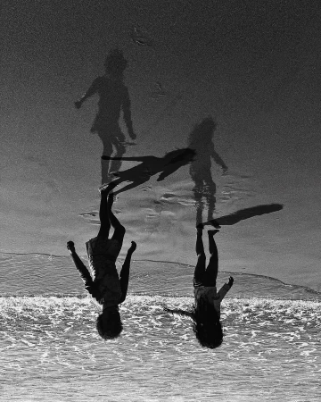 Monochrome photo of children playing on a beach with breaking waves and wet sand, in an upside-down composition.