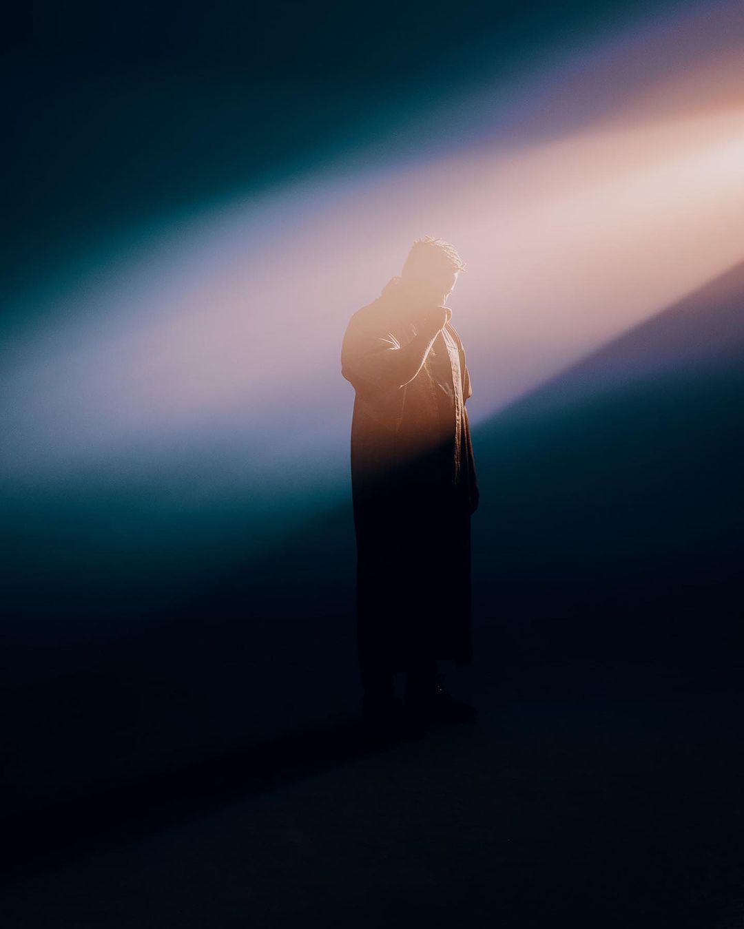 Silhouette of a person standing in a dramatic beam of light against a dark background, photographed by Bethany Mollenkof.