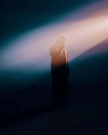 Silhouette of a person standing in a dramatic beam of light against a dark background, photographed by Bethany Mollenkof.