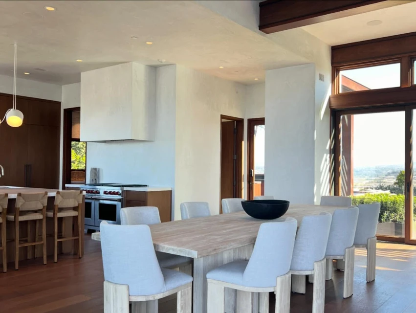 Dining area featuring a long wooden table with light blue chairs, set in a naturally lit room with a view and modern decor.