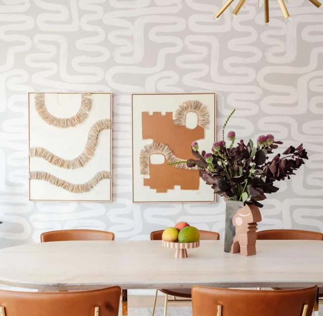 Home interior features abstract artwork on walls, oval dining table with fruit, stylish chairs, and decorative ceramic object.
