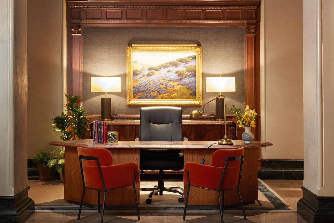 Office interior features wooden desk with chairs, lamps, clock, books, and artwork, creating a professional and decorative workspace.