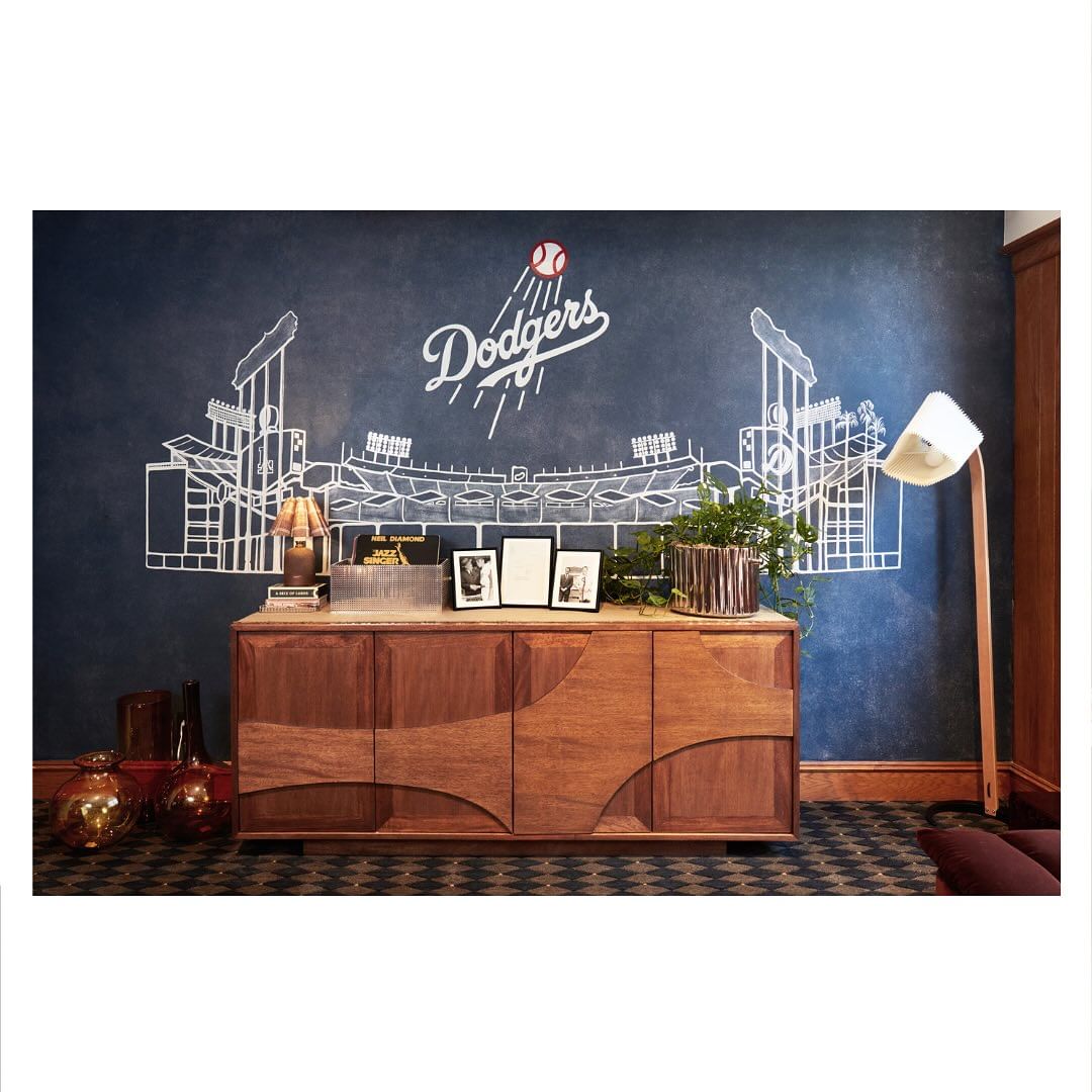 Living room interior with a wooden sideboard, floor lamp, and a wall mural of the Dodgers stadium painted in white lines on a blue wall.