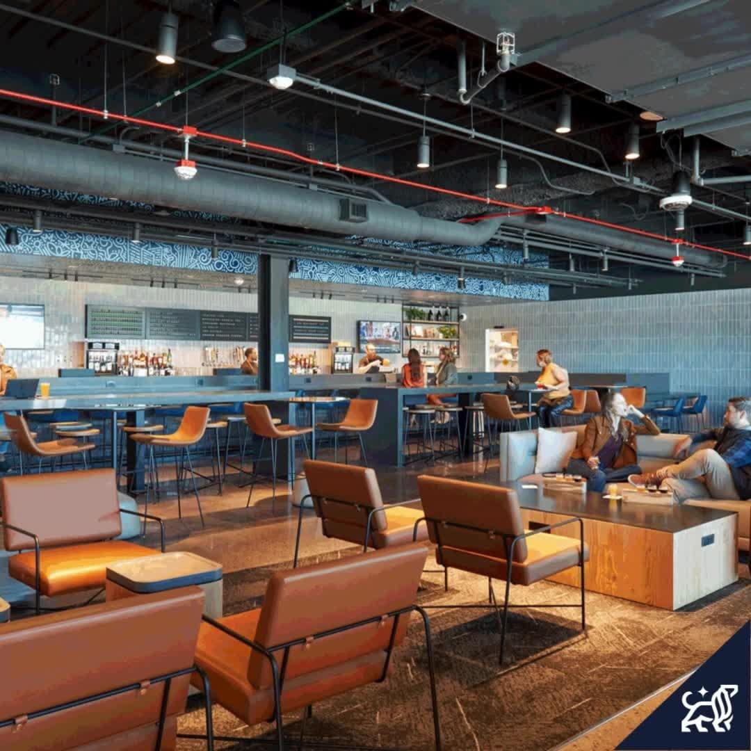 Indoor view of a bar and lounge area with people seated at the bar and in lounge chairs, with modern industrial design.