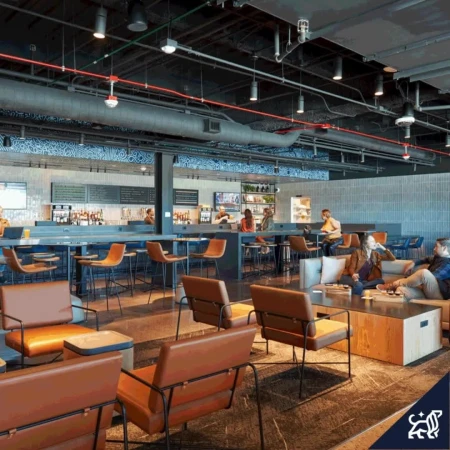 Indoor view of a bar and lounge area with people seated at the bar and in lounge chairs, with modern industrial design.