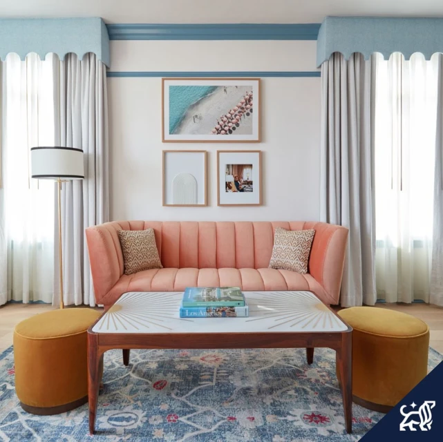 Interior shot of a seating area with a velvet couch, patterned rug, and coffee table with books in a well-lit room.