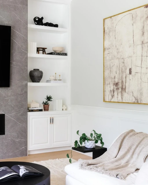 Living room interior featuring a white sofa, black coffee table with books, built-in white shelving, and a minimalist painting.