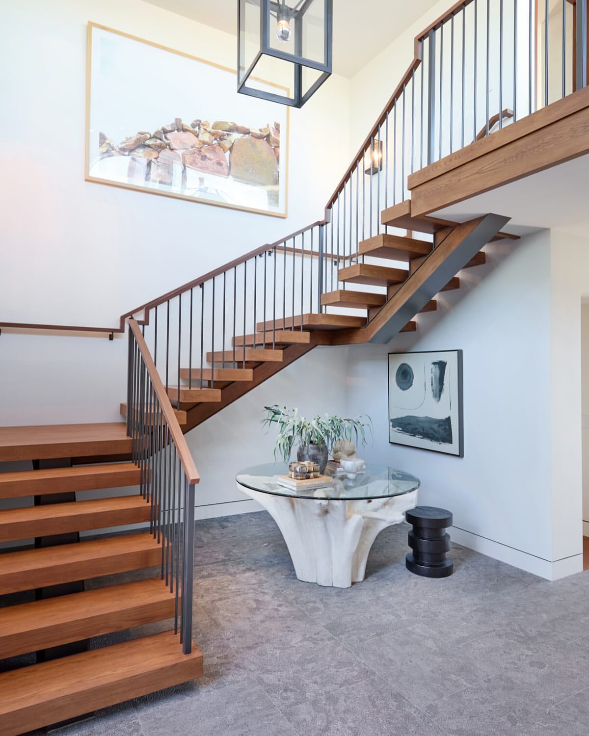 Interior view of a modern home entryway featuring floating wood stairs with metal railings and a glass-topped table with a wood base.
