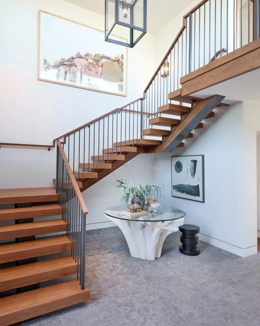 Interior view of a modern home entryway featuring floating wood stairs with metal railings and a glass-topped table with a wood base.
