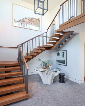 Interior view of a modern home entryway featuring floating wood stairs with metal railings and a glass-topped table with a wood base.