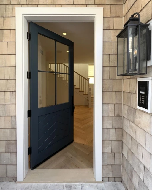 Exterior shot of an open blue door with glass panes, white trim, and cedar shake siding, providing a glimpse into the interior of a home.