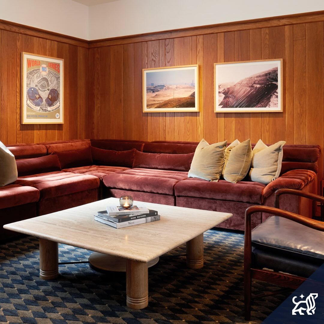 Living room with a maroon sectional sofa, light wood paneling, framed prints, a square marble coffee table, and patterned blue rug.