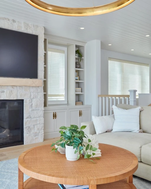 Living room interior featuring a fireplace with television, round wooden coffee table, and a cream-colored sofa with neutral decor.