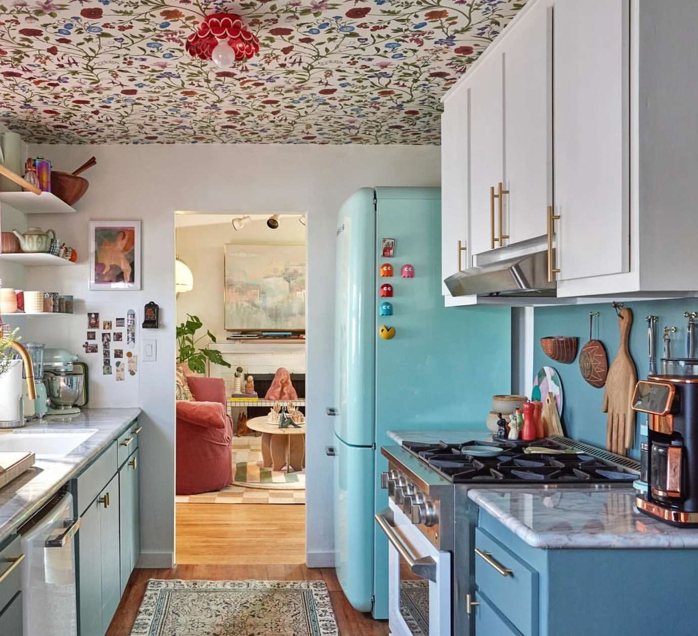 Pastel kitchen interior featuring robin's egg blue retro refrigerator, gas stove, white cabinets, floral ceiling, and vintage decor.