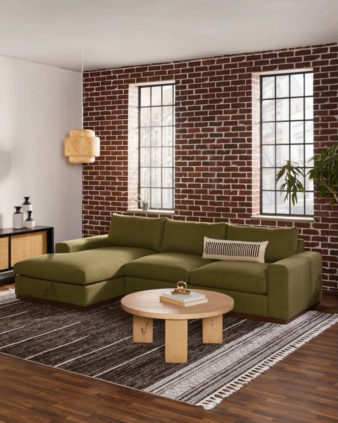 Interior living room features a sectional sofa in olive green, a round coffee table, and a striped rug against a brick accent wall.