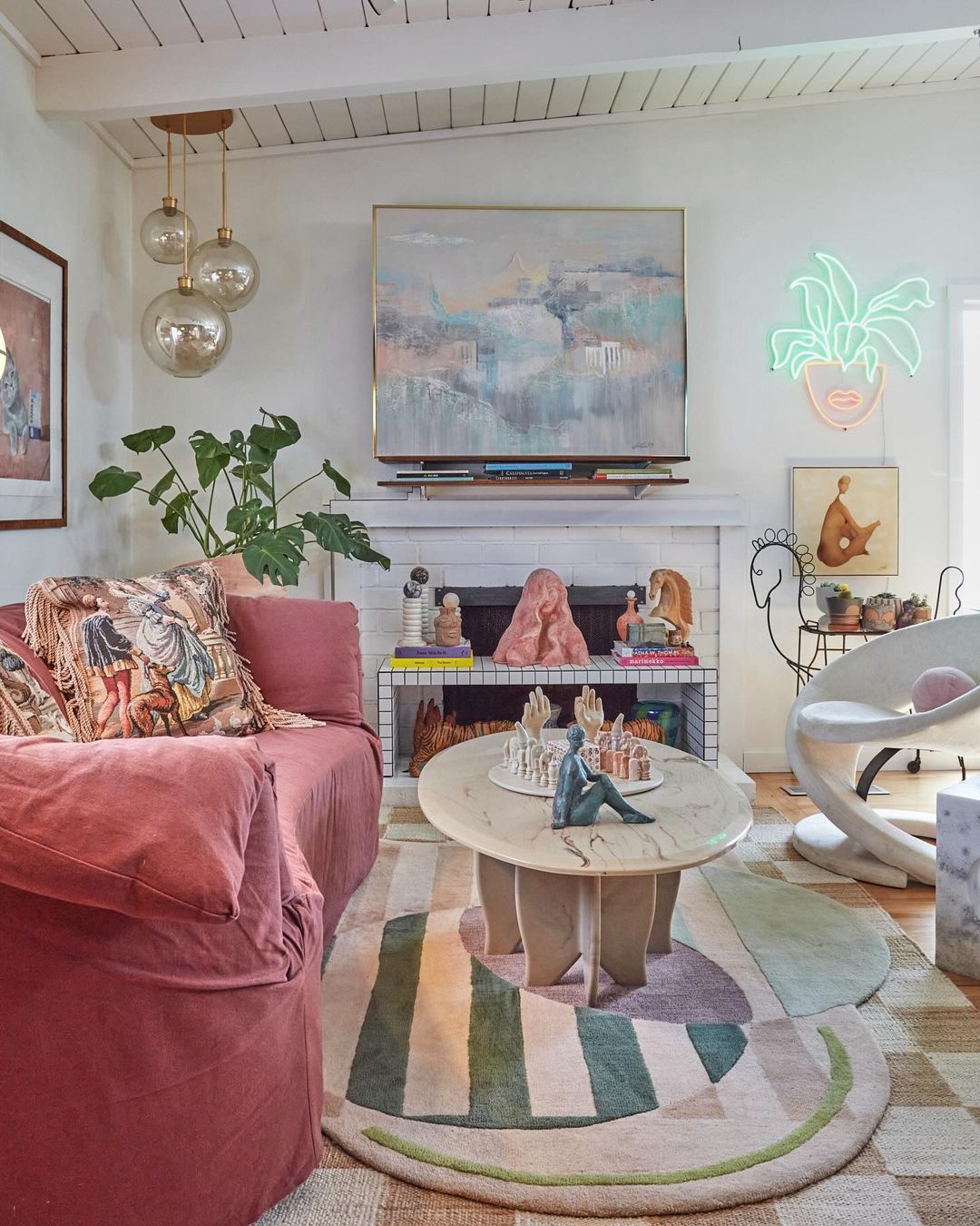 Eclectic living room interior featuring a pink sofa, patterned rug, artwork, and decorative objects, creating a cozy, vintage-inspired space.