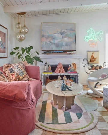 Eclectic living room interior featuring a pink sofa, patterned rug, artwork, and decorative objects, creating a cozy, vintage-inspired space.