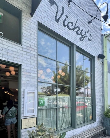 Exterior of Vicky's restaurant featuring white brick, large windows with reflections, and a view of the interior with patrons.