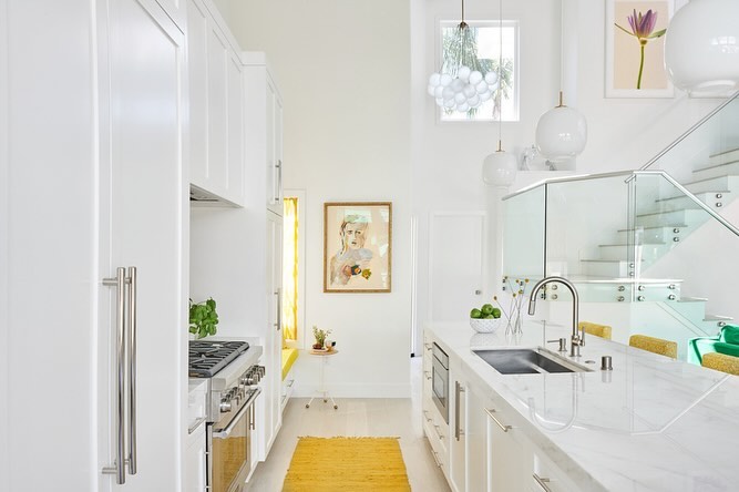 Bright, modern kitchen with white cabinets, countertops, stainless steel appliances, and decor, including a woven yellow rug.