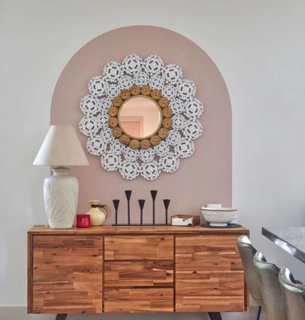 Interior with wooden cabinet, table lamp, decorative wall mirror, and candle holder, creating a cozy and elegant home decor scene.