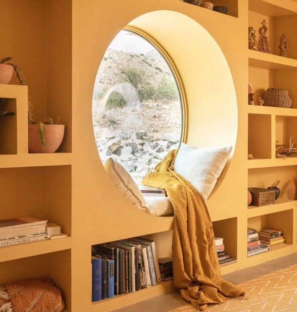Cozy reading nook with a round window showcasing a desert landscape, featuring built-in bookshelves and a golden yellow color scheme.