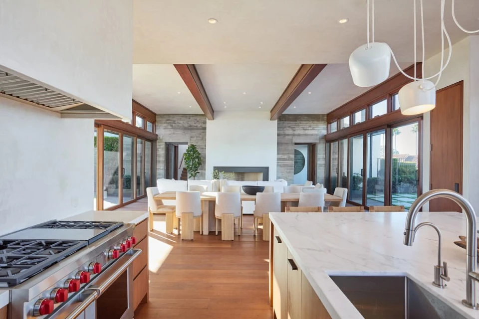 Open-concept modern interior view of a living and dining space featuring wooden floors, an island kitchen, and exterior windows.