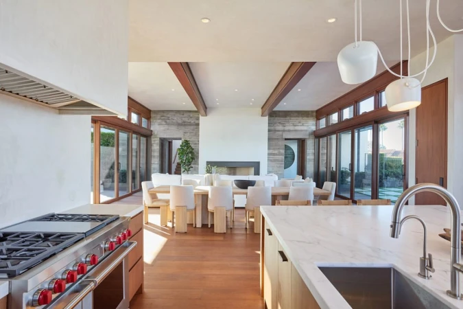 Open-concept modern interior view of a living and dining space featuring wooden floors, an island kitchen, and exterior windows.