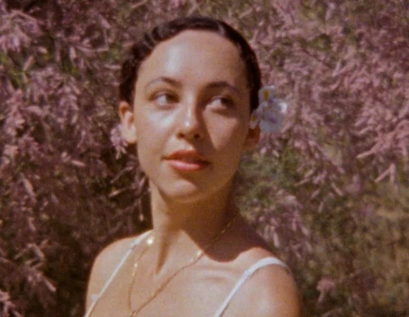 Portrait of a woman with a flower in her dark hair standing in front of blooming pink blossoms