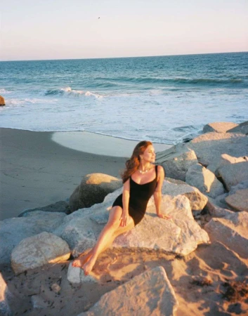 Woman in a black dress seated on coastal rocks by the ocean at sunset, photographed by Bethany Reed.