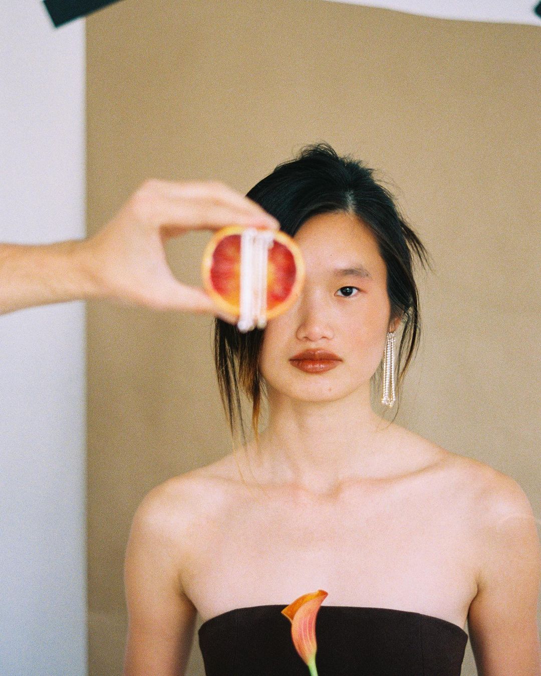 Woman poses with sliced orange and calla lily in a studio setting. The image features a blend of beauty and artistic composition.