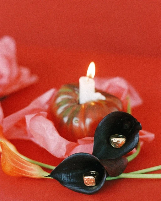 Floral arrangement with black calla lilies and a pumpkin candle on a red surface, conveying a moody and elegant ambiance.