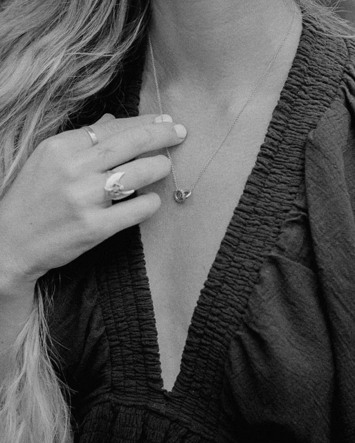 Close-up studio shot of a person wearing a silver necklace and rings, showcasing jewelry against a dark, textured garment.