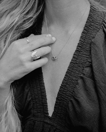 Close-up studio shot of a person wearing a silver necklace and rings, showcasing jewelry against a dark, textured garment.
